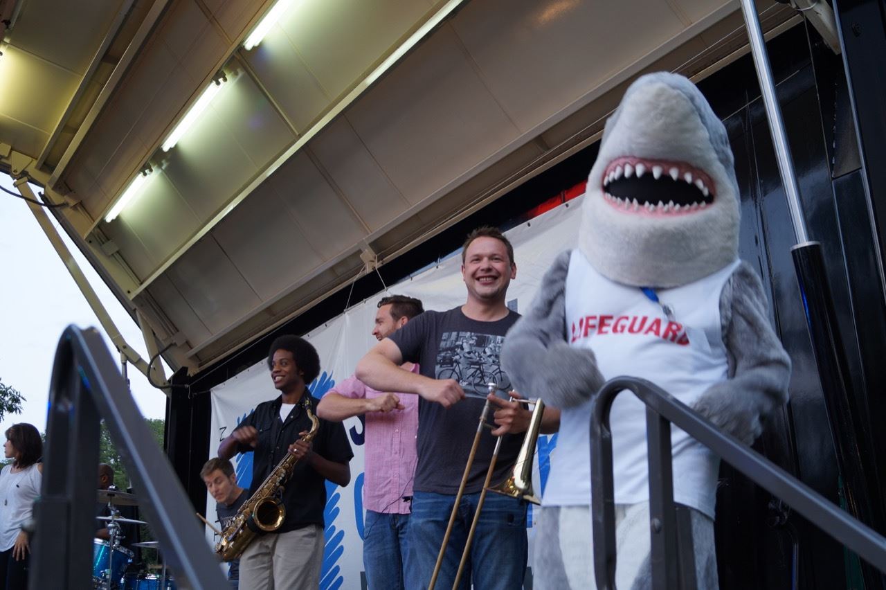 Shark mascot plays the air trombone with members of the band.